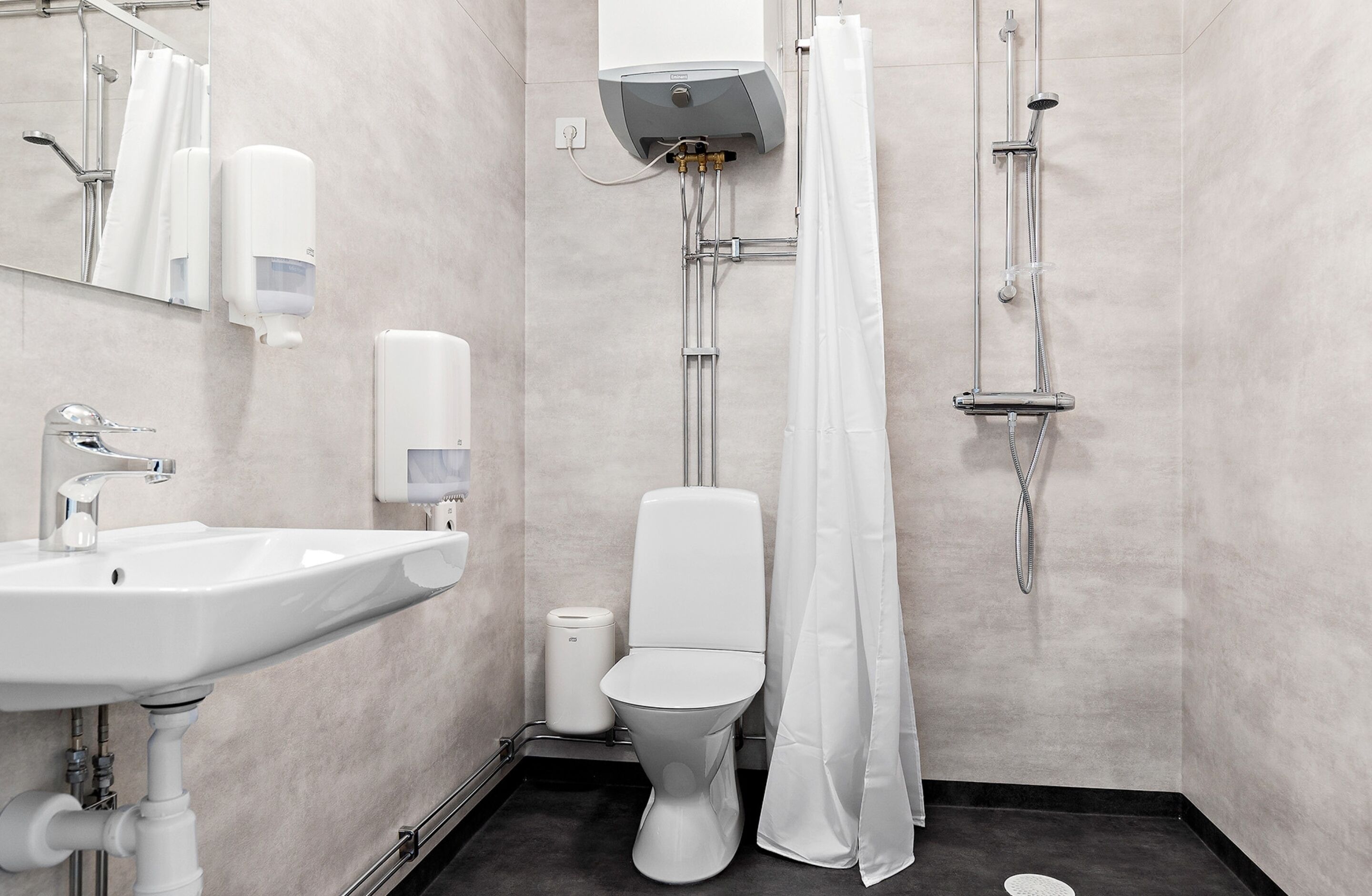 A modern bathroom with a sink, toilet, shower, and hand dryer.