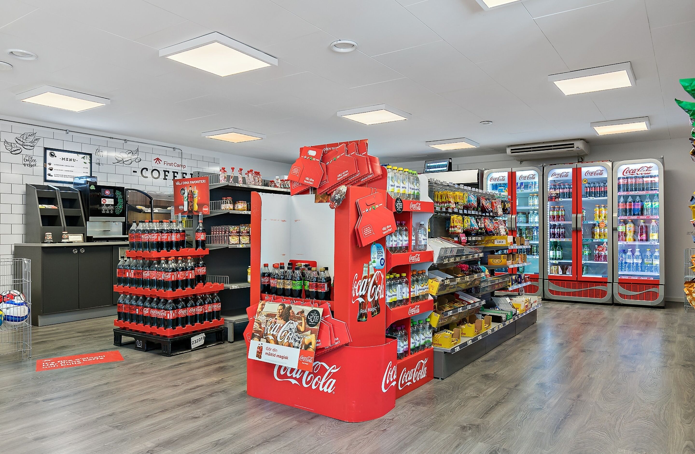 A store interior with Coca-Cola displays, refrigerated sections, and a coffee station.