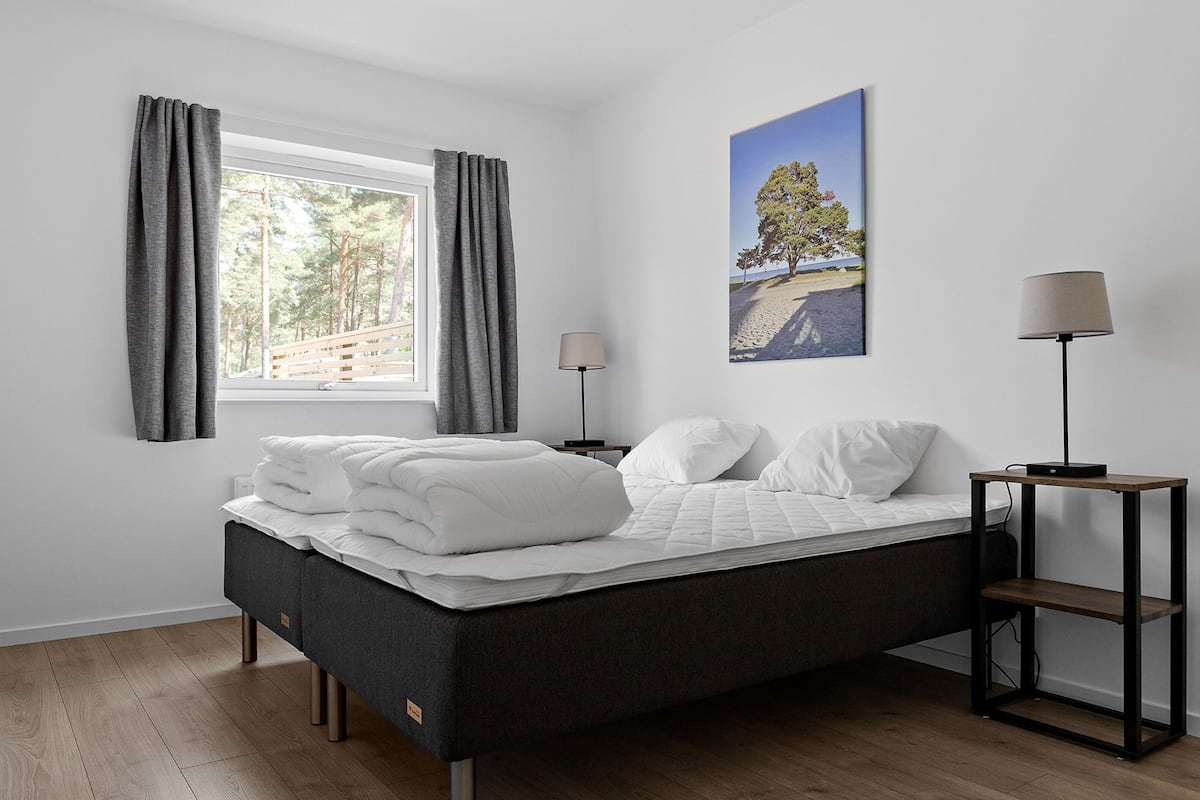 Un lit bien fait, avec du linge de lit blanc, une table de chevet avec une lampe et une fenêtre avec des rideaux.