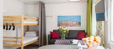 A compact room with bunk beds, a sofa, a dining table, and a TV.