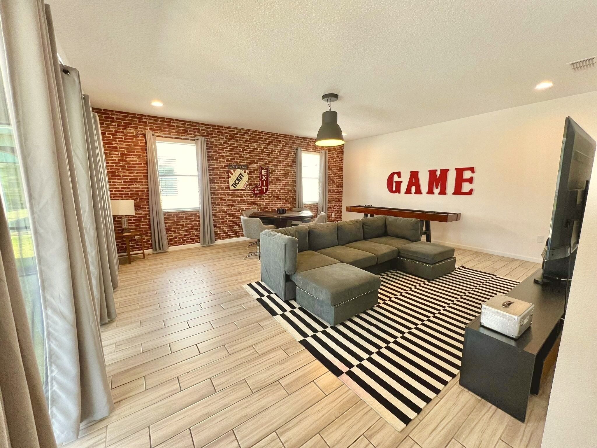 A modern living room with a sectional sofa, a black and white striped rug, a television, and a wall with the word "GAME" in red letters.