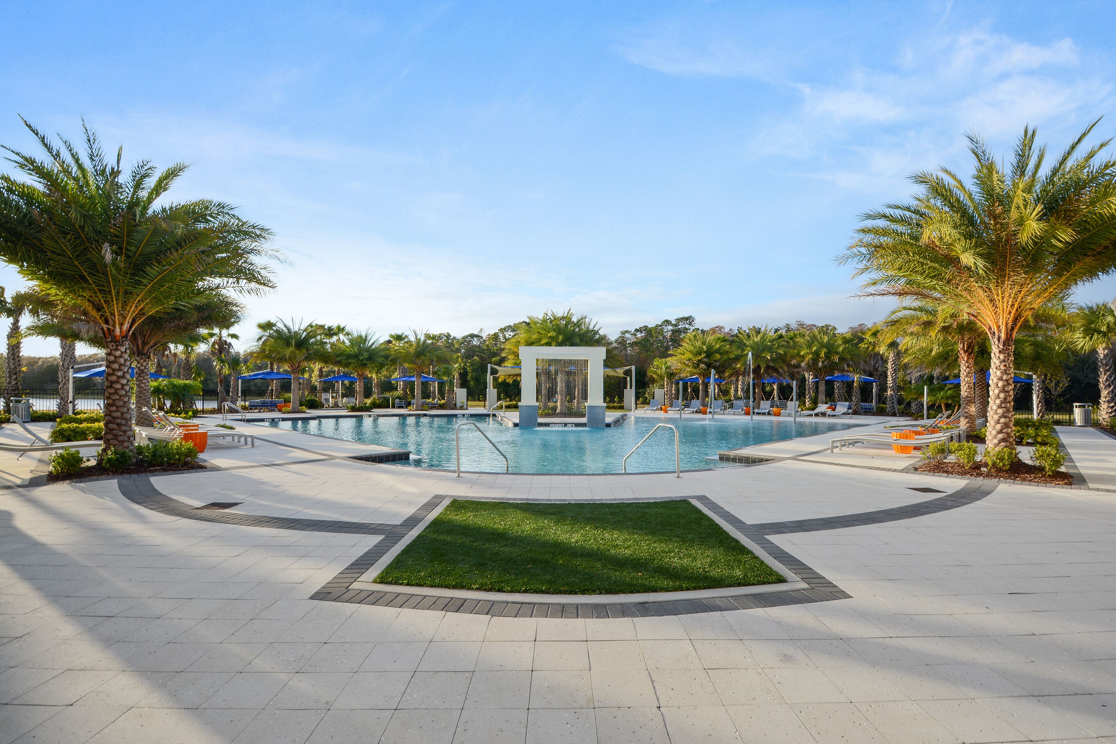 A swimming pool area with palm trees, lounge chairs, and a small waterfall feature.