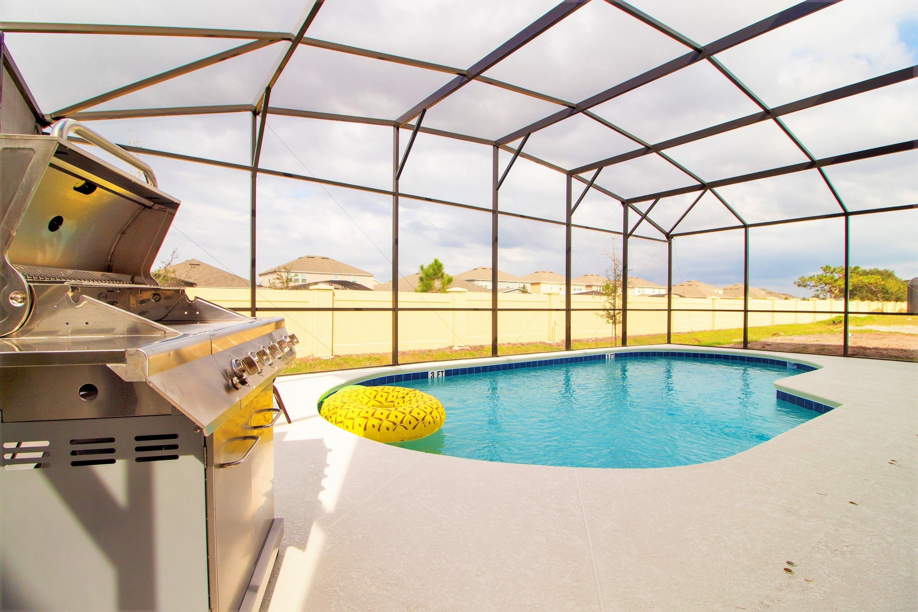 An outdoor swimming pool with a yellow inflatable ring, a barbecue grill, and a metal roof structure.