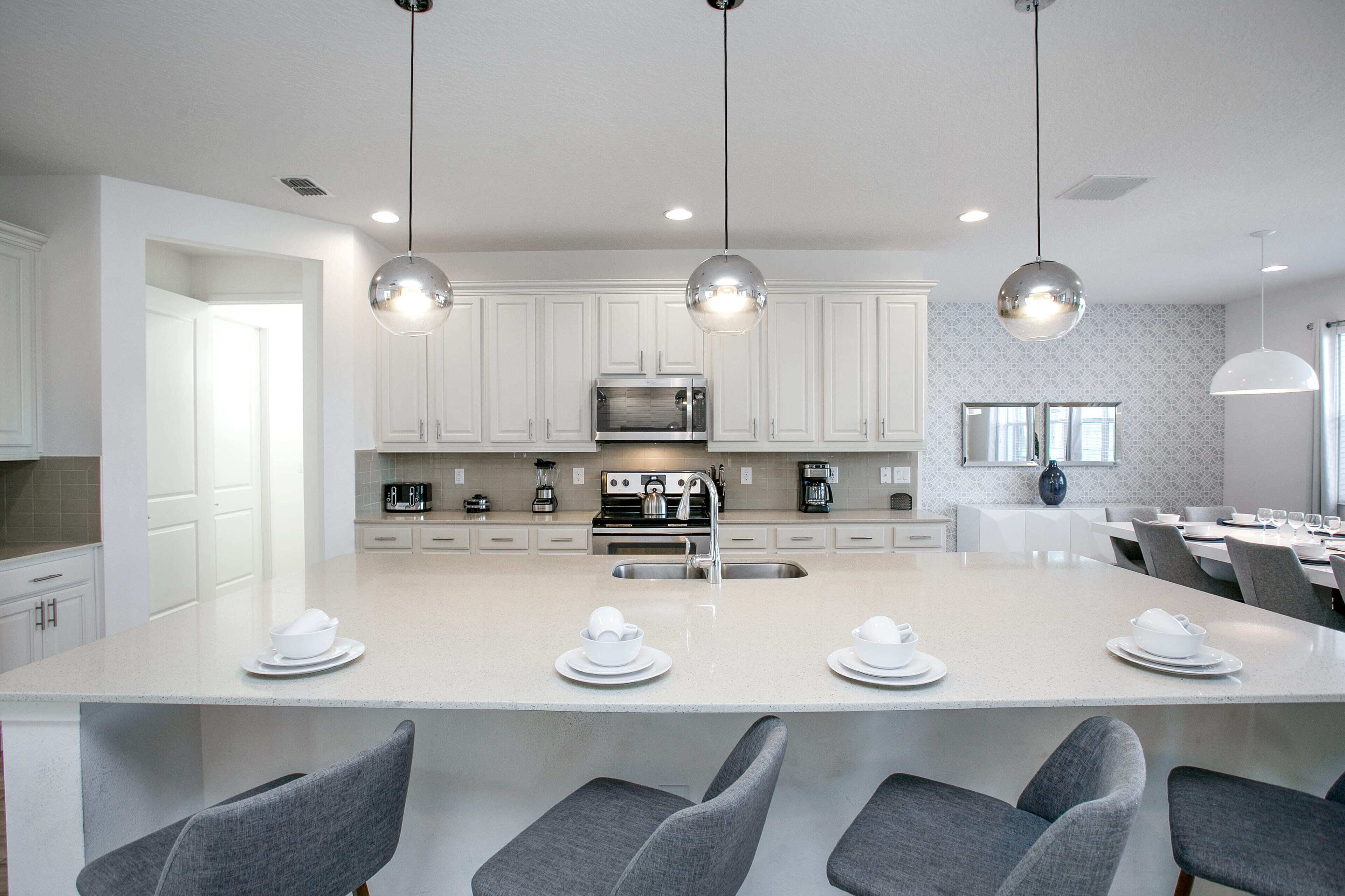 A modern kitchen with white cabinets, a large island with bar seating, stainless steel appliances, and pendant lighting.
