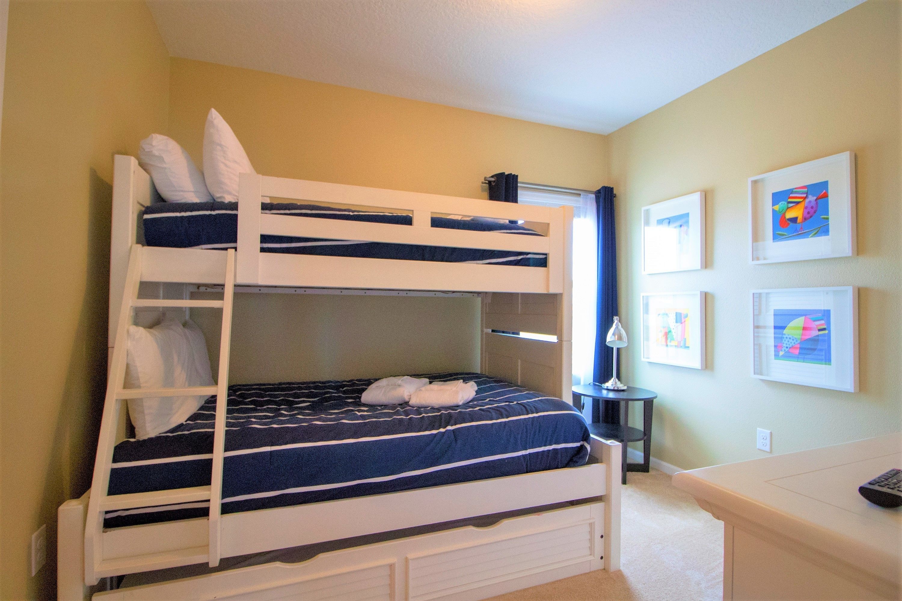 Una cama individual superpuesta con escritorio y silla, una lámpara y cuadros en la pared.
