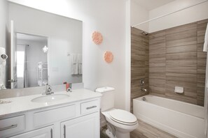 A bathroom with a white sink, toilet, and bathtub. There are decorative wall flowers and a shower curtain. - Sonoma Resort (Kissimmee)