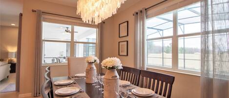 A dining area with a wooden table set for four, two vases with white flowers, and a chandelier.