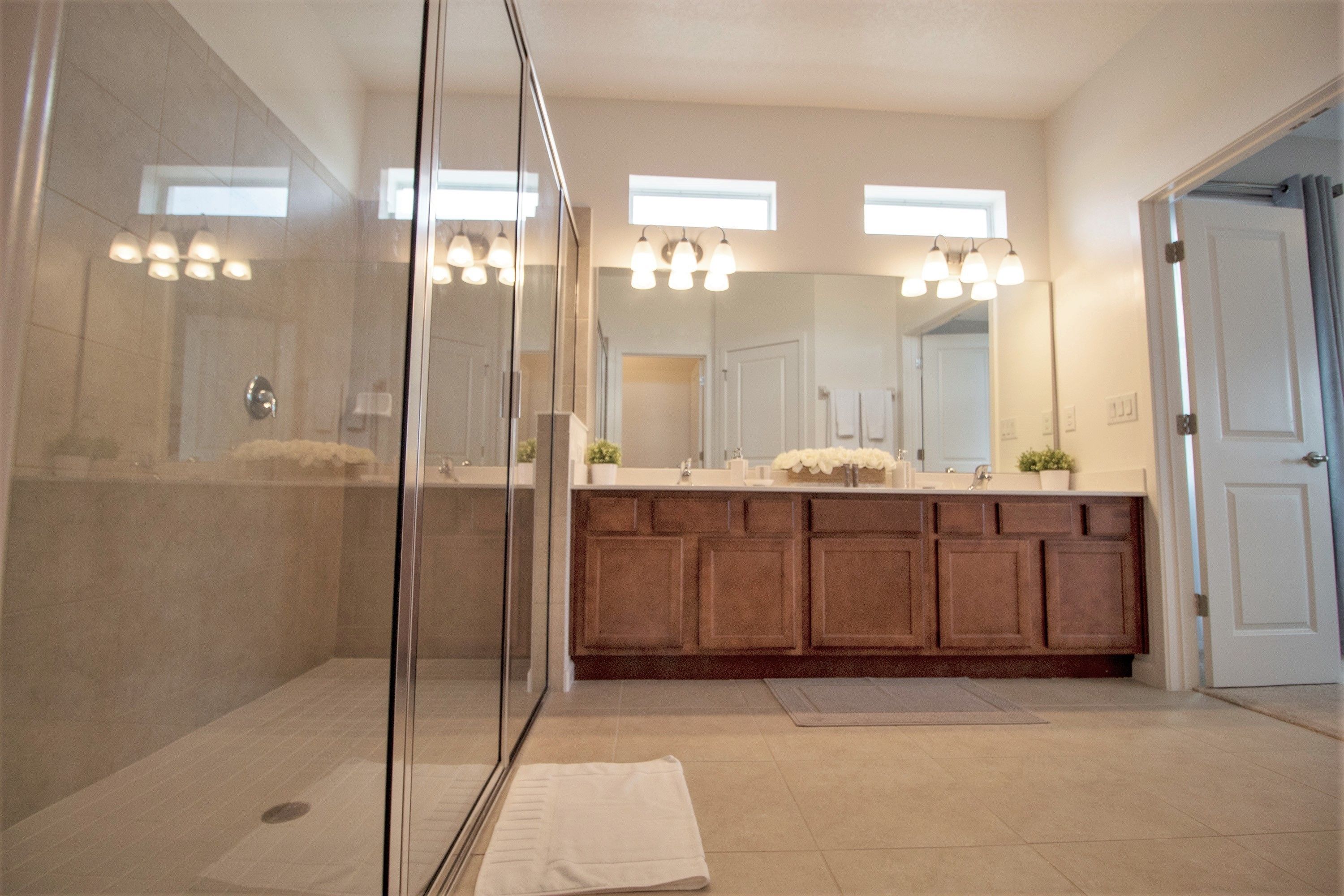 A modern bathroom with a glass shower enclosure, a large mirror, and a wooden vanity.