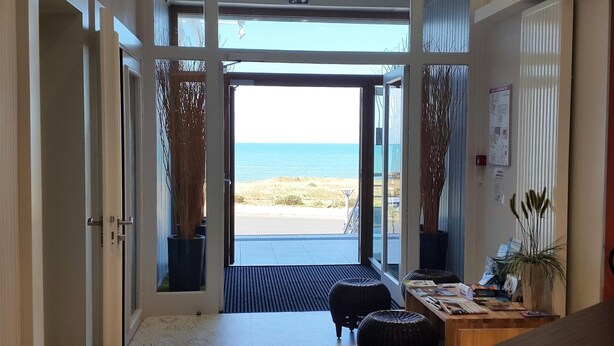 A room with a view of the beach, a desk with papers, and a chair.