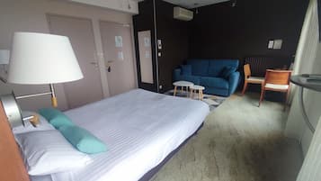 A hotel room with a bed, a desk, a chair, a blue sofa, and a lamp.