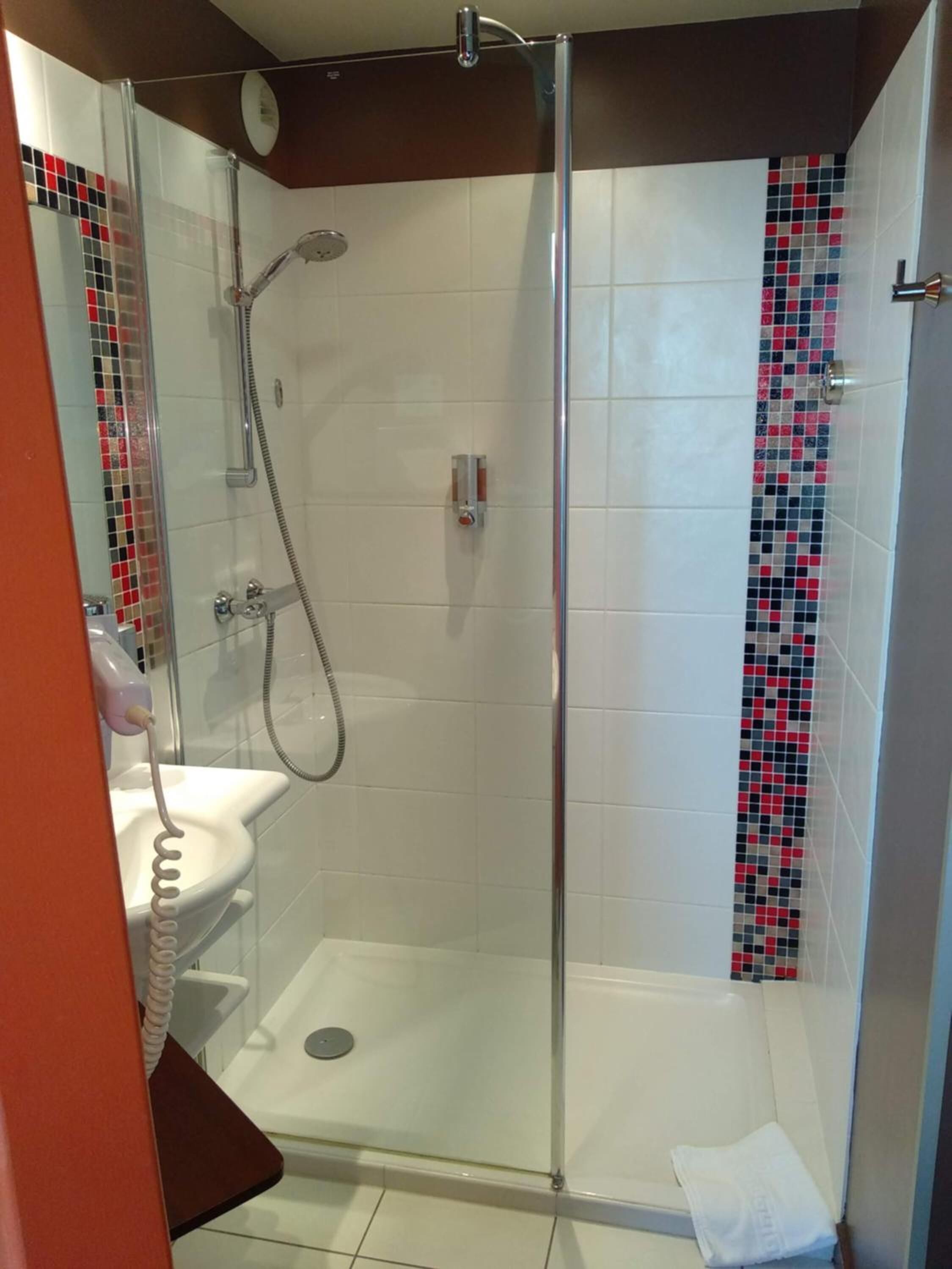 A glass-enclosed shower with a white sink and a handheld showerhead.