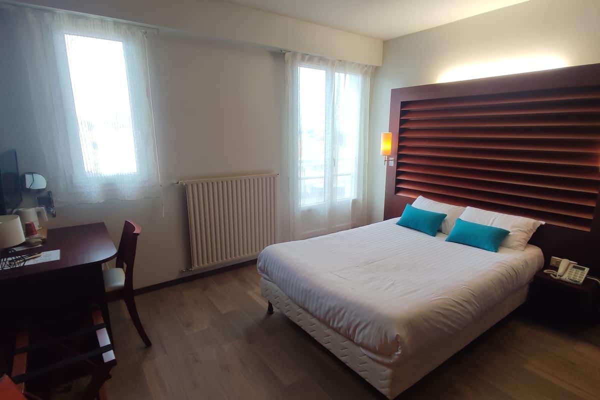 Ein Hotelzimmer mit einem großen Bett, einem Schreibtisch, einem Sessel, einem Heizkörper und einem Telefon.