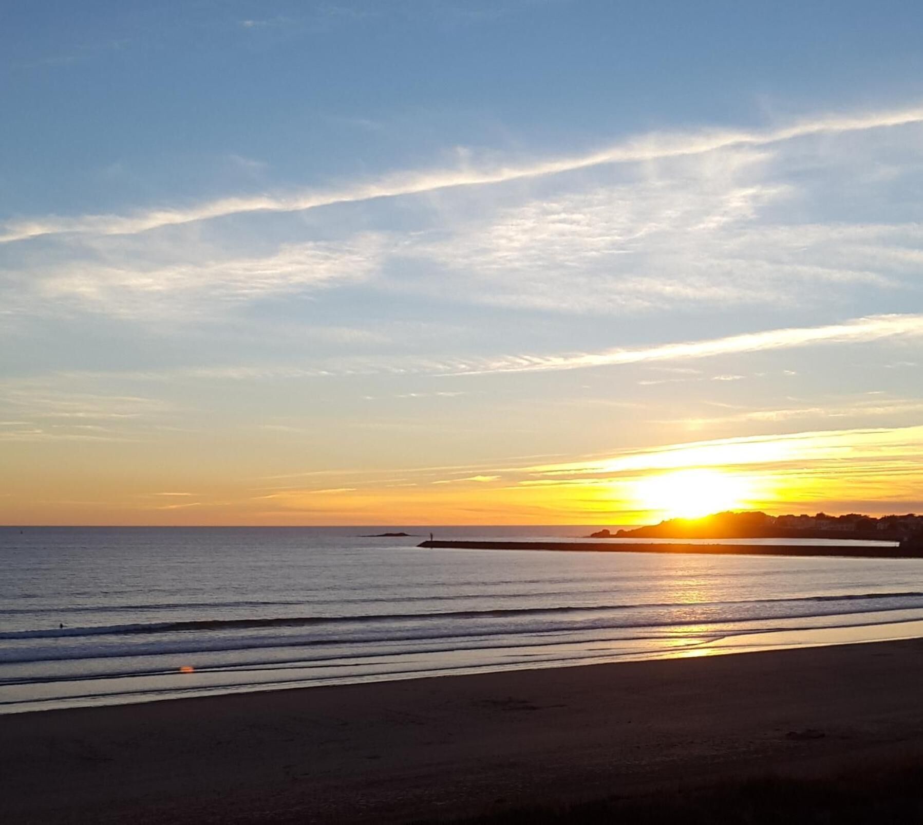 A beach with a sunset, calm sea, and a distant pier.