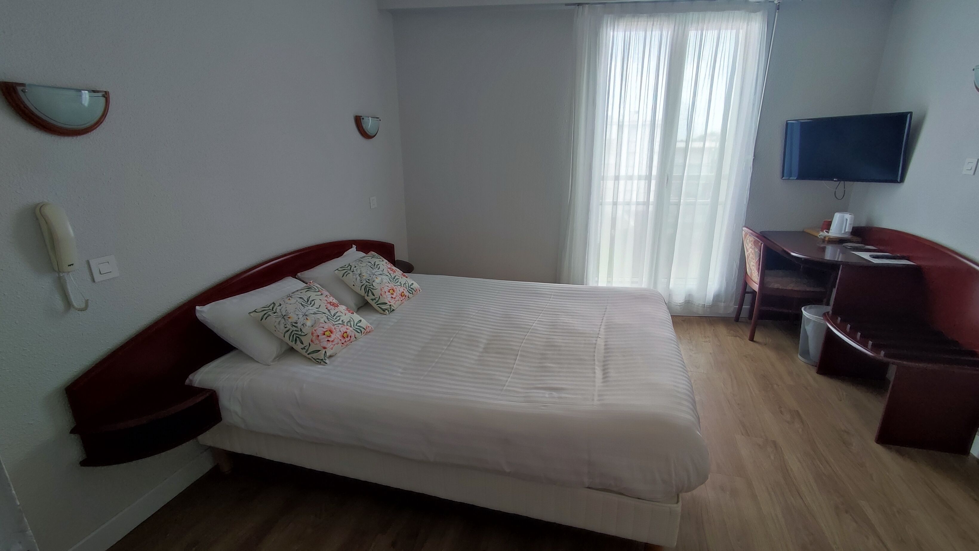 A hotel room with a bed, a desk, a chair, a TV, and a telephone.