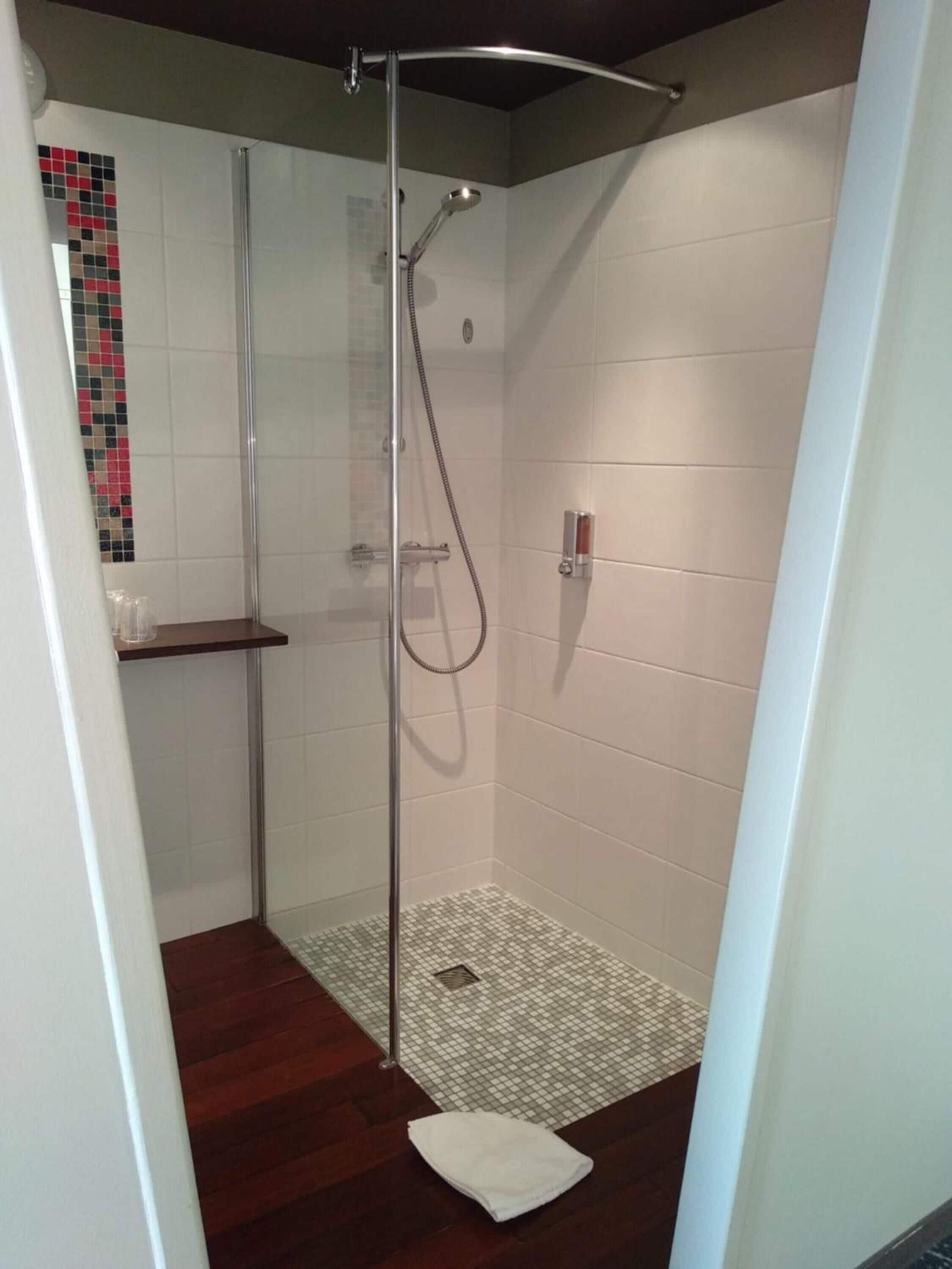 Een douche met glazen wanden, een betegelde vloer, een plank en een wandbeugel voor handdoeken.