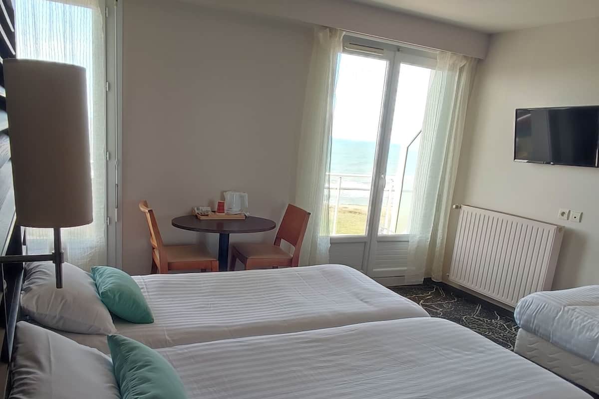 Ein Hotelzimmer mit zwei Betten, einem Tisch mit Stühlen, einem Fernseher und Meerblick.