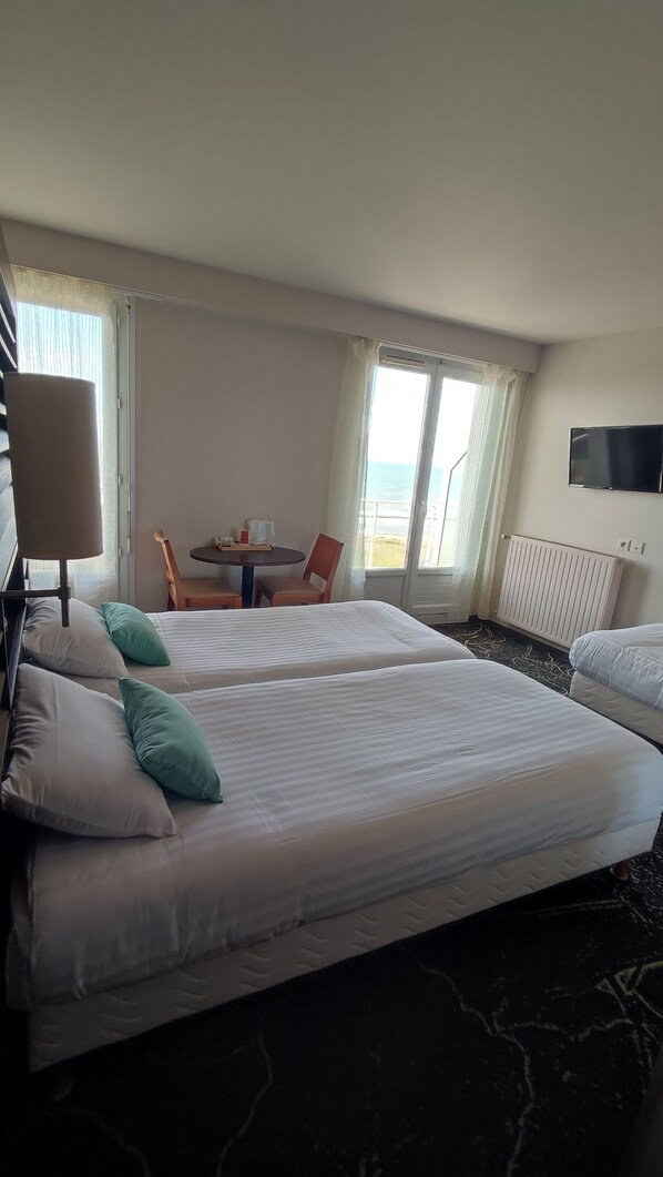 A hotel room with two beds, a table with chairs, a TV, and a view of the sea. - Hôtel La Corniche (Saint-Hilaire-de-Riez)