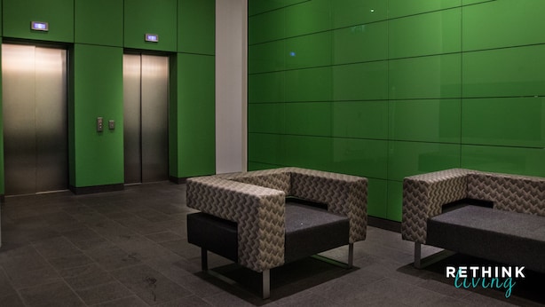 A lobby with green walls, two elevators, and two patterned seating areas. - Rethink Living - Hewitt Tower (Reading)