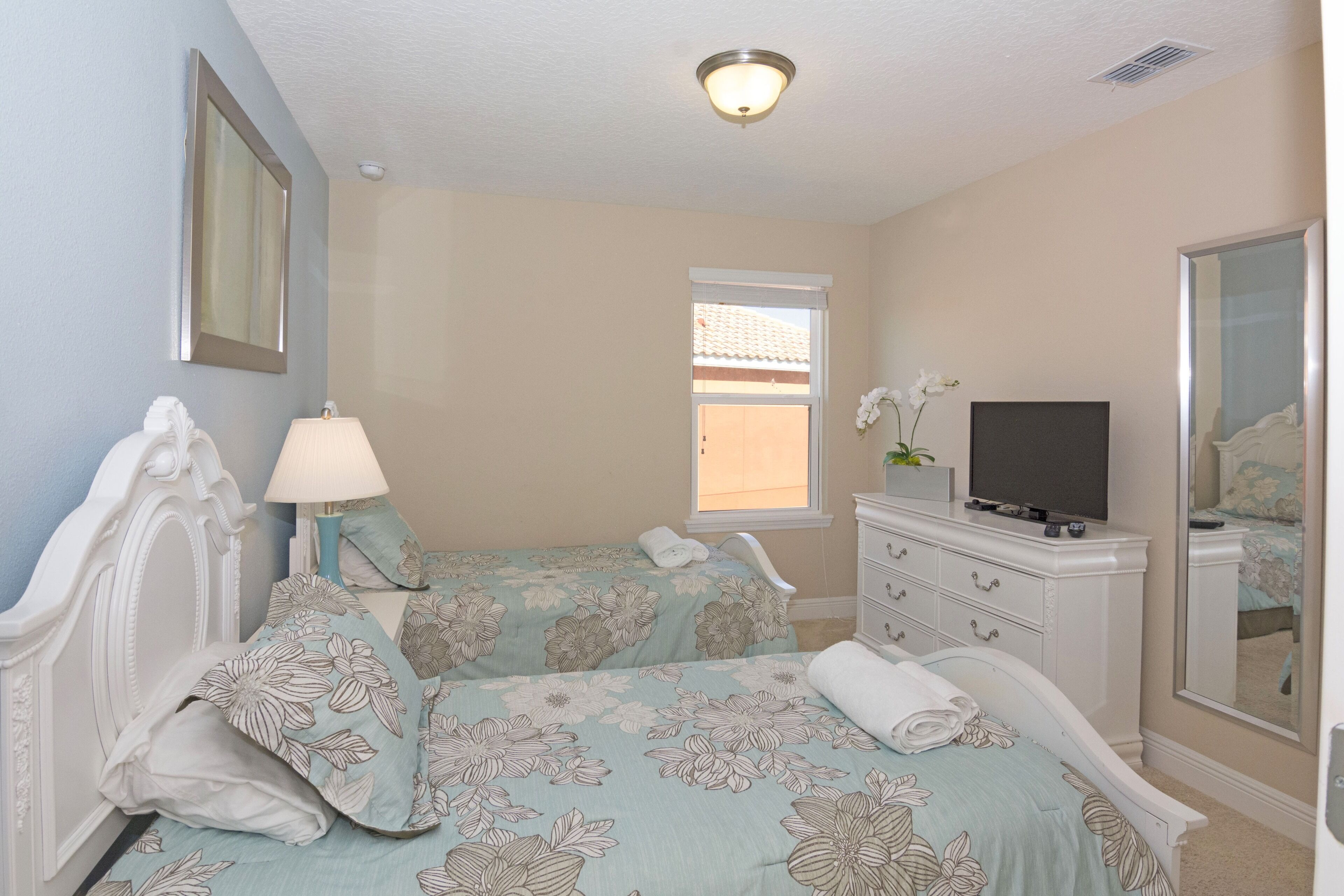A bedroom with two beds, a dresser, a television, and a window.