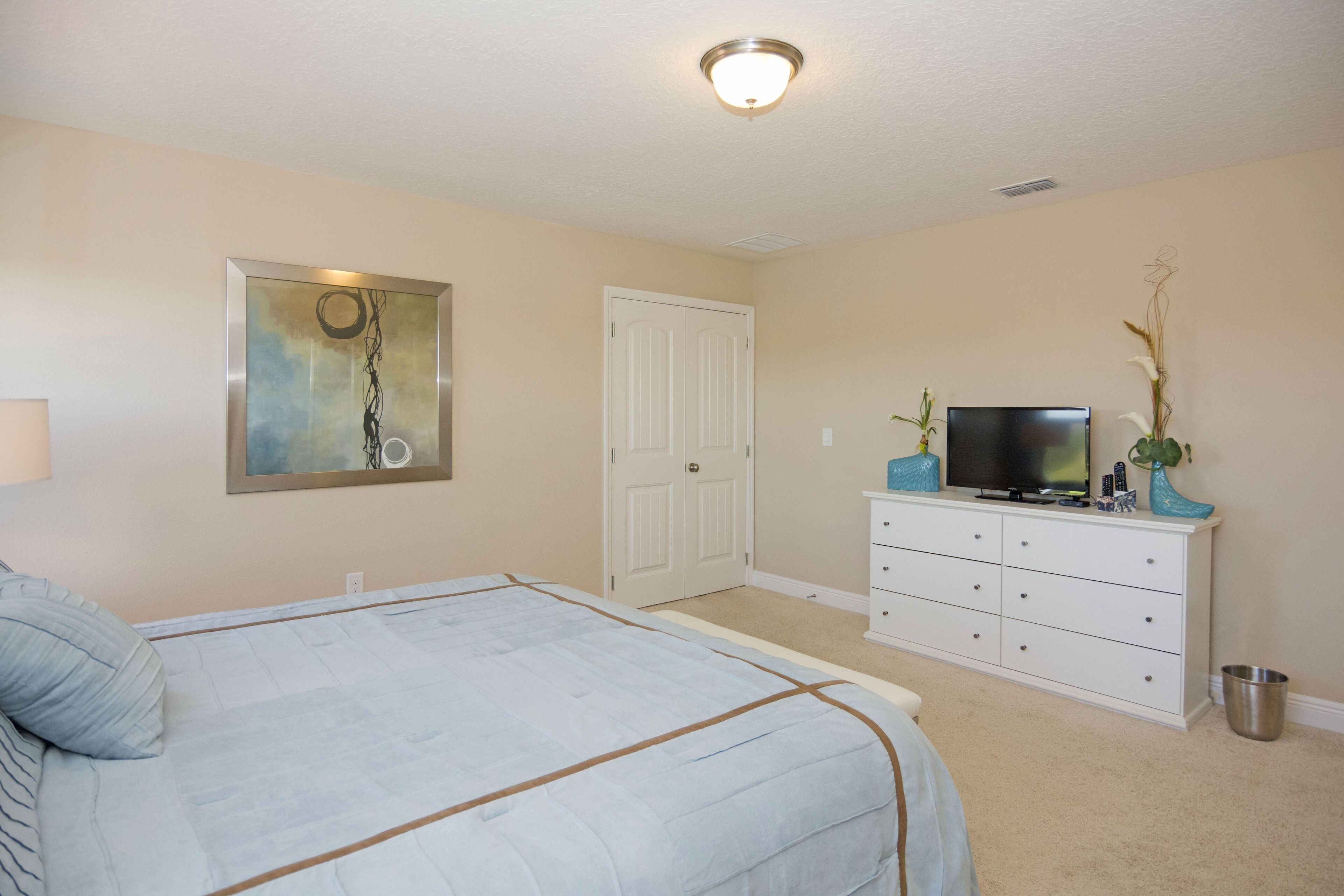 A bedroom with a bed, a dresser, a television, and a door.