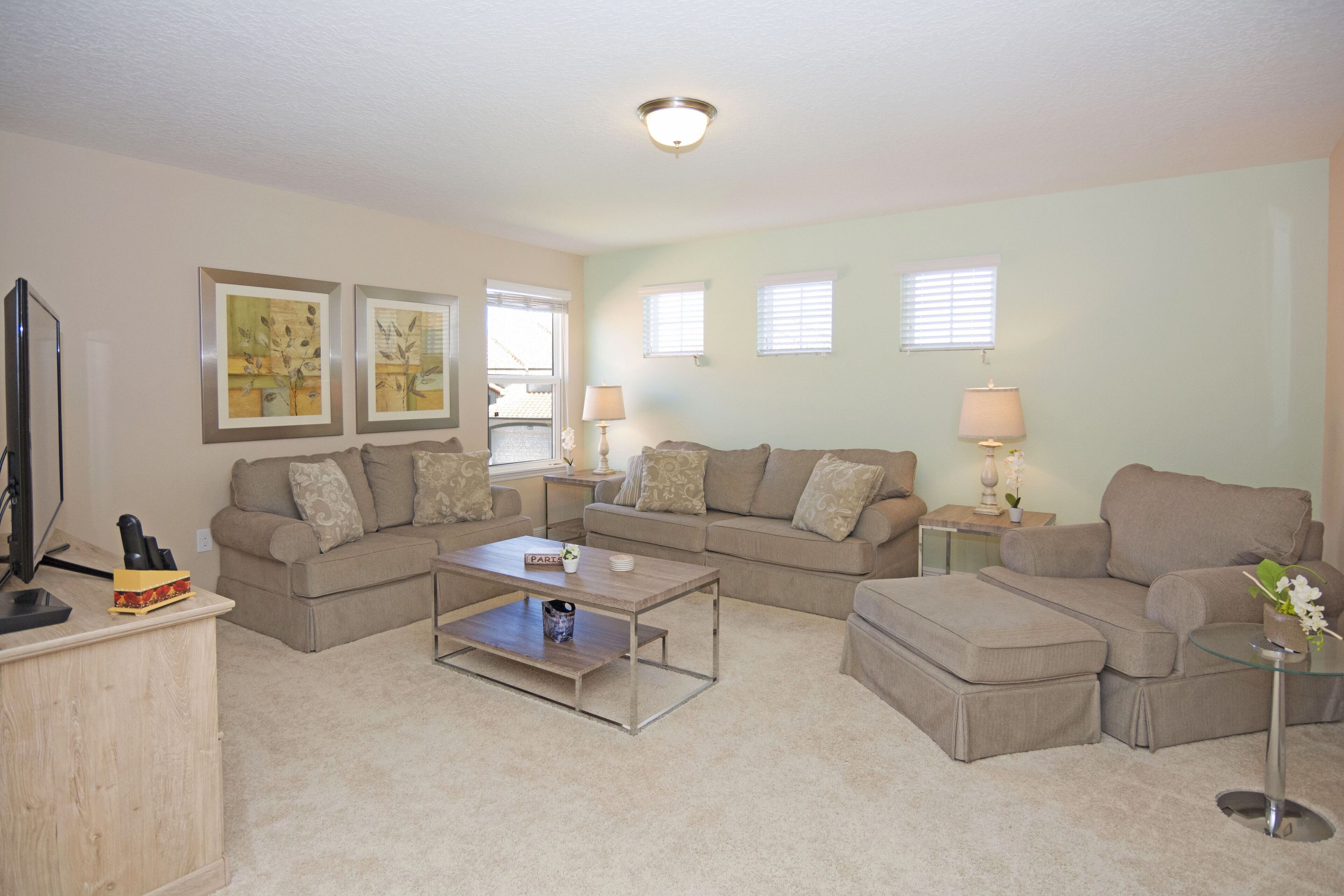 A living room with a sectional sofa, a coffee table, a TV, and artwork on the walls.