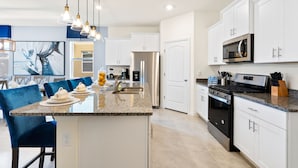 A modern kitchen with white cabinets, a stainless steel refrigerator, a built-in oven, and a granite countertop. - Solterra Resort (Davenport)