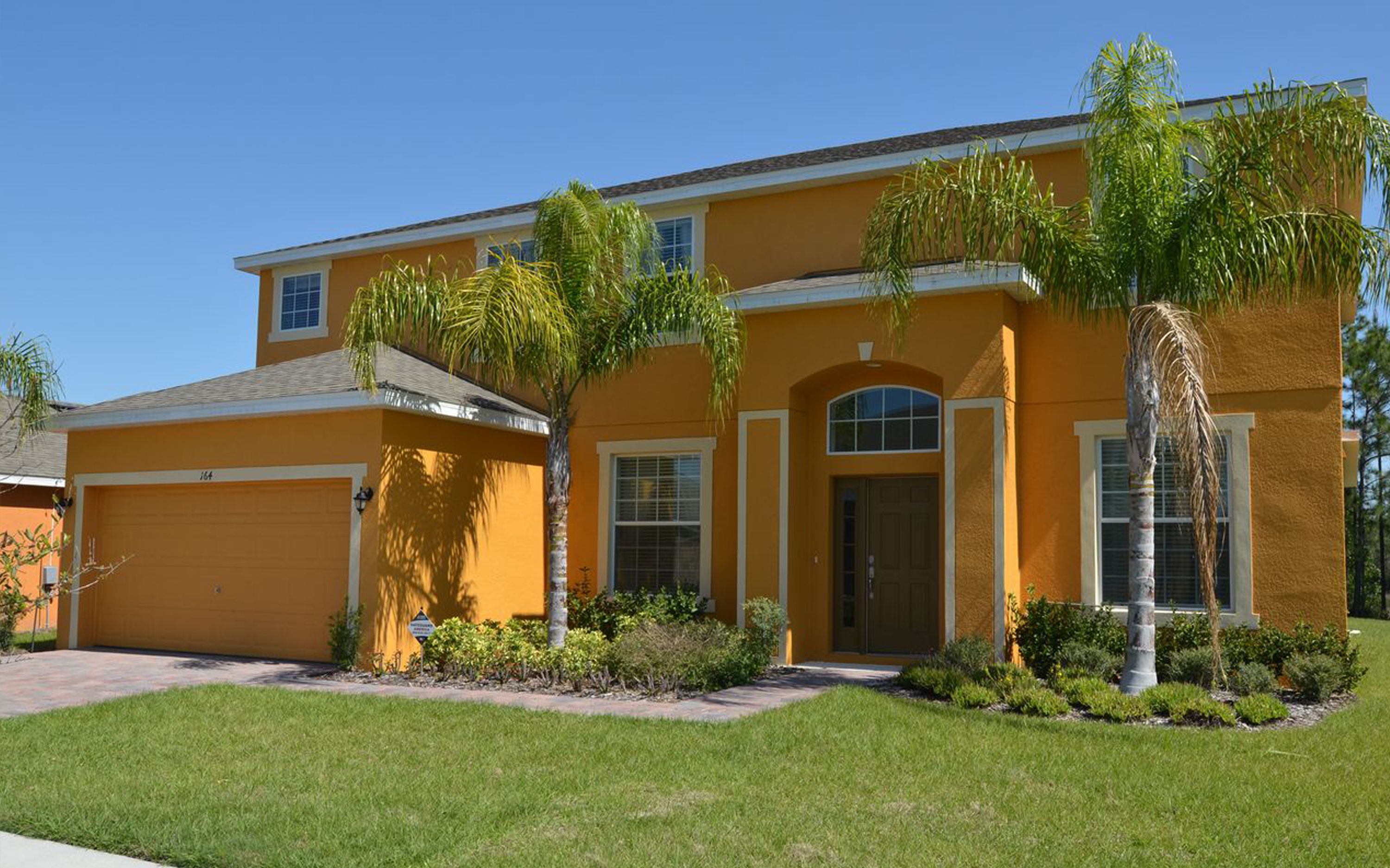 A two-story house with a yellow exterior, a garage, and a well-maintained lawn.