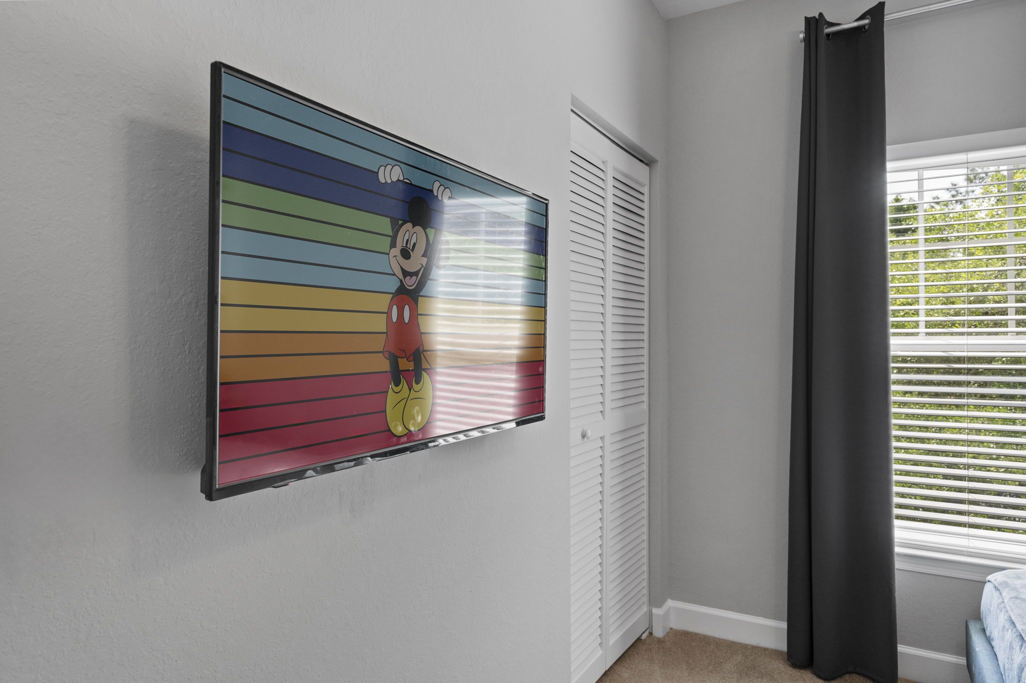 A room with a large colorful poster on the wall, a window with blinds, and a door with louvered shutters.