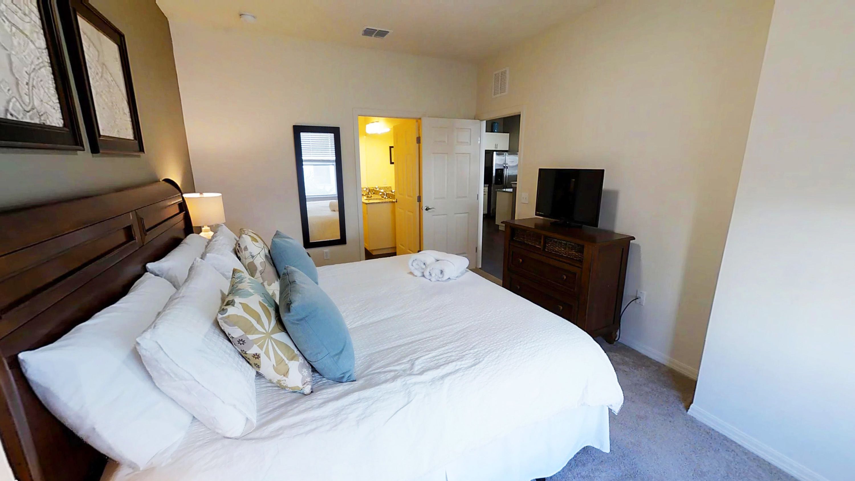 A hotel room with a large bed, a dresser, a television, and a bathroom visible through an open door.