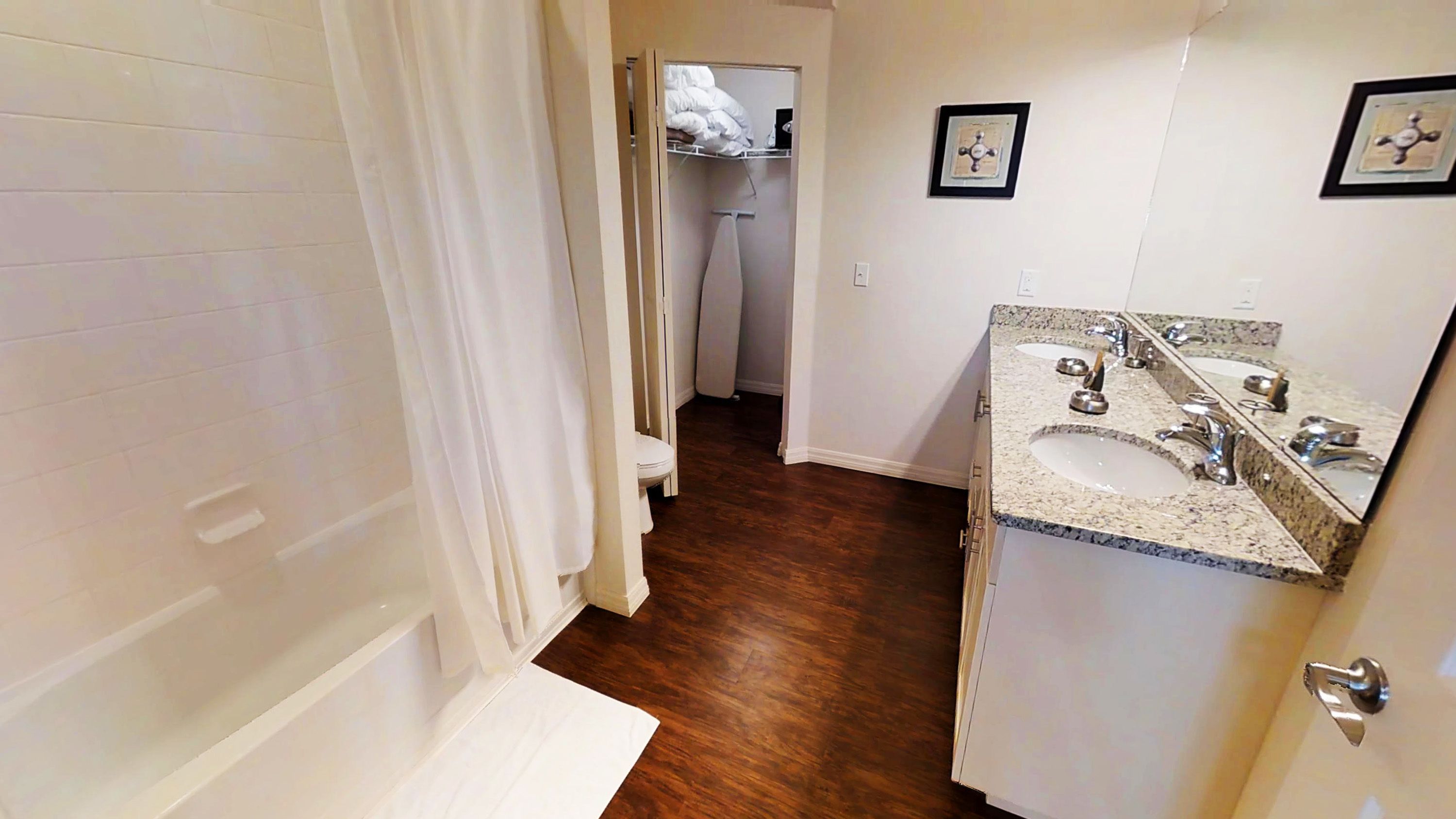 Un baño con tocador doble lavamanos, inodoro y vestidor con un tendedero.