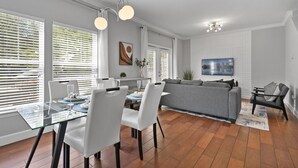 A modern living room with a glass dining table, white chairs, a grey sofa, and a black armchair. There is a painting on the wall and a ceiling light fixture. - Lucaya Vacation Homes (Kissimmee)