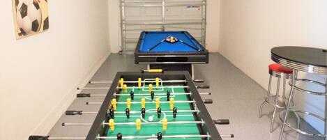 A foosball table in a room with a metal gate and a bar stool.