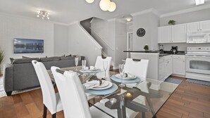 A modern kitchen with white cabinets, a microwave, and a stove. There is a dining area with a glass table and white chairs. - Lucaya Vacation Homes (Kissimmee)