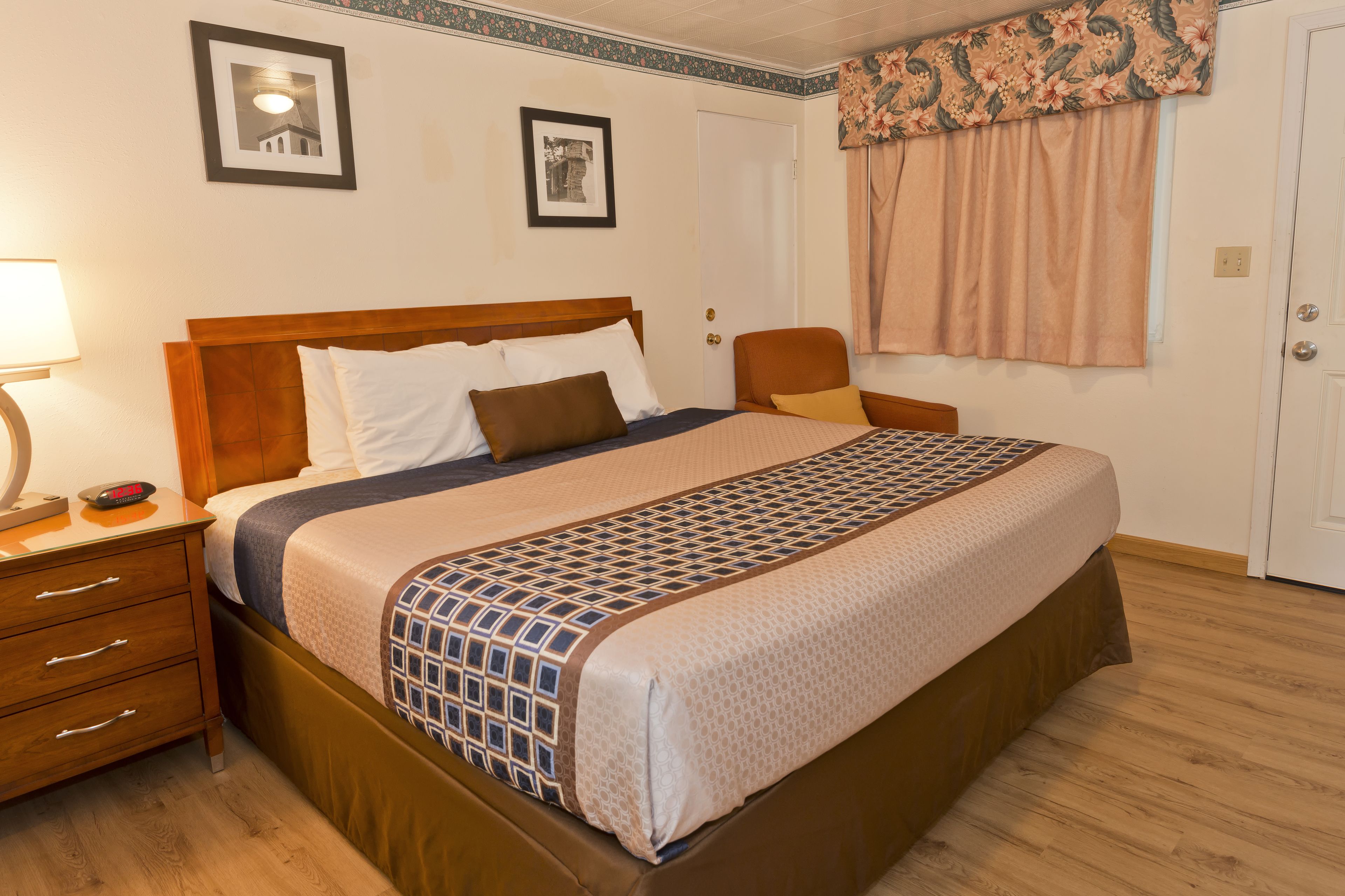 A neatly made bed with a patterned bedspread, a bedside table with a lamp, and two framed pictures on the wall.