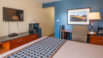 Ein Hotelzimmer mit einem Bett, einem Flachbildfernseher, einer Mikrowelle, einem Schreibtisch, einem Sessel und einem gerahmten Bild an der Wand.
