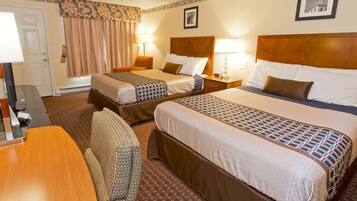 A hotel room with two beds, a desk, a chair, and a door.
