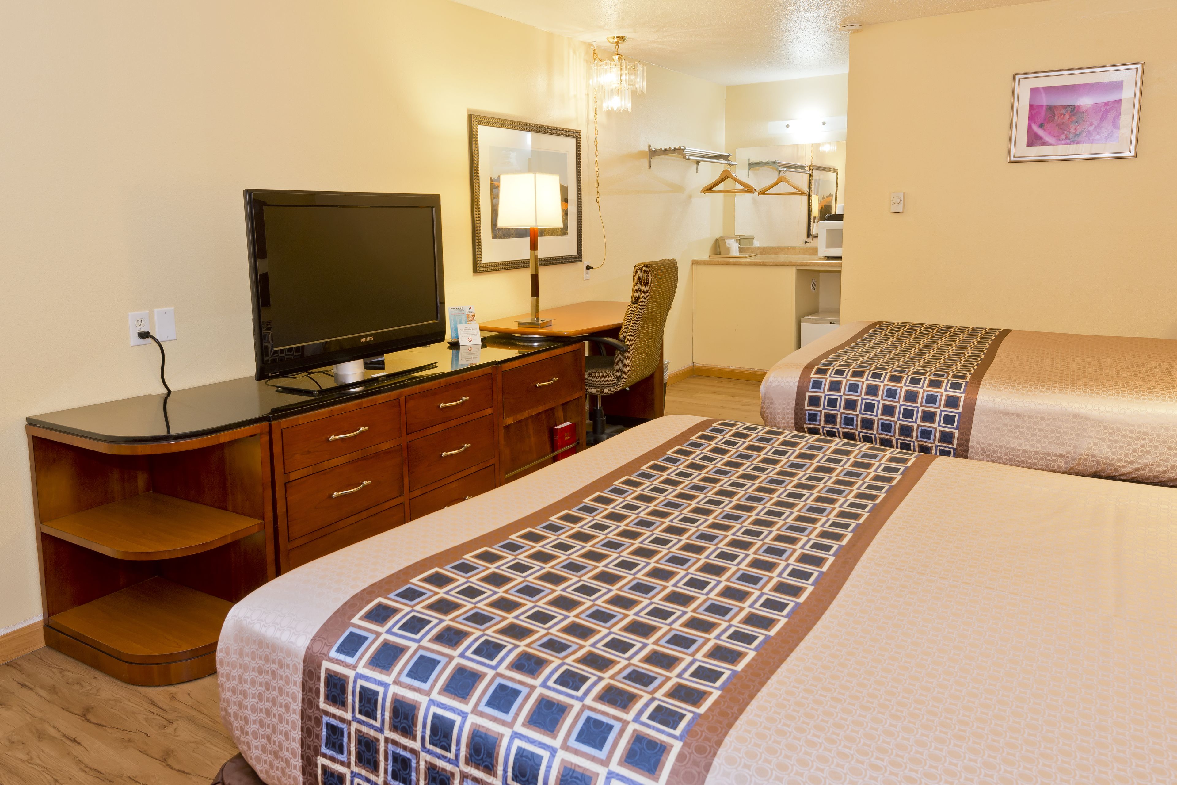 A hotel room with a TV, desk, chair, and two beds with patterned bedspreads.