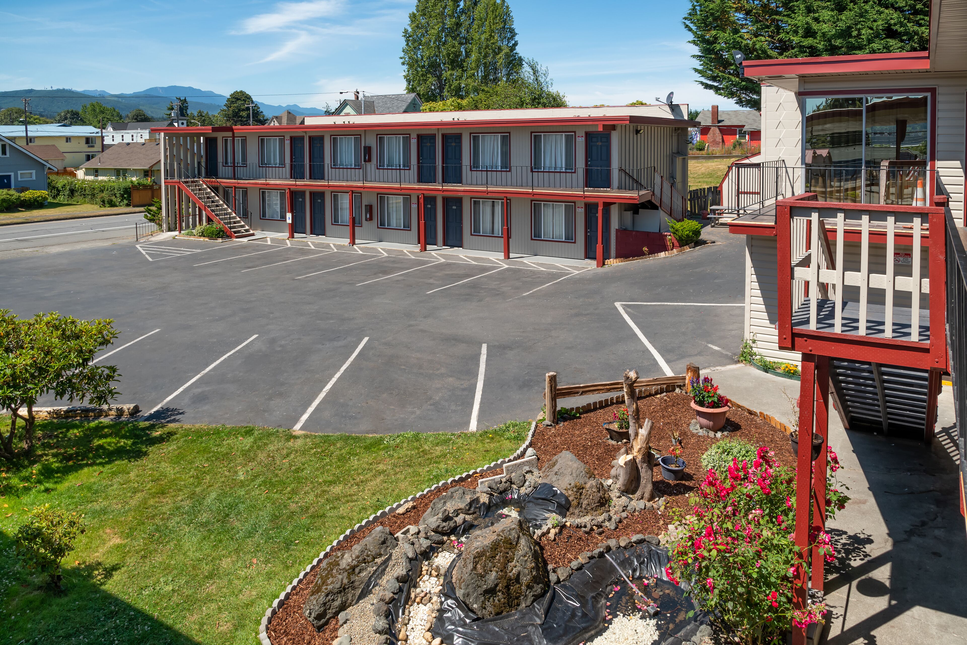 A motel with a parking lot, a small garden area with rocks and plants, and a staircase leading to the entrance.