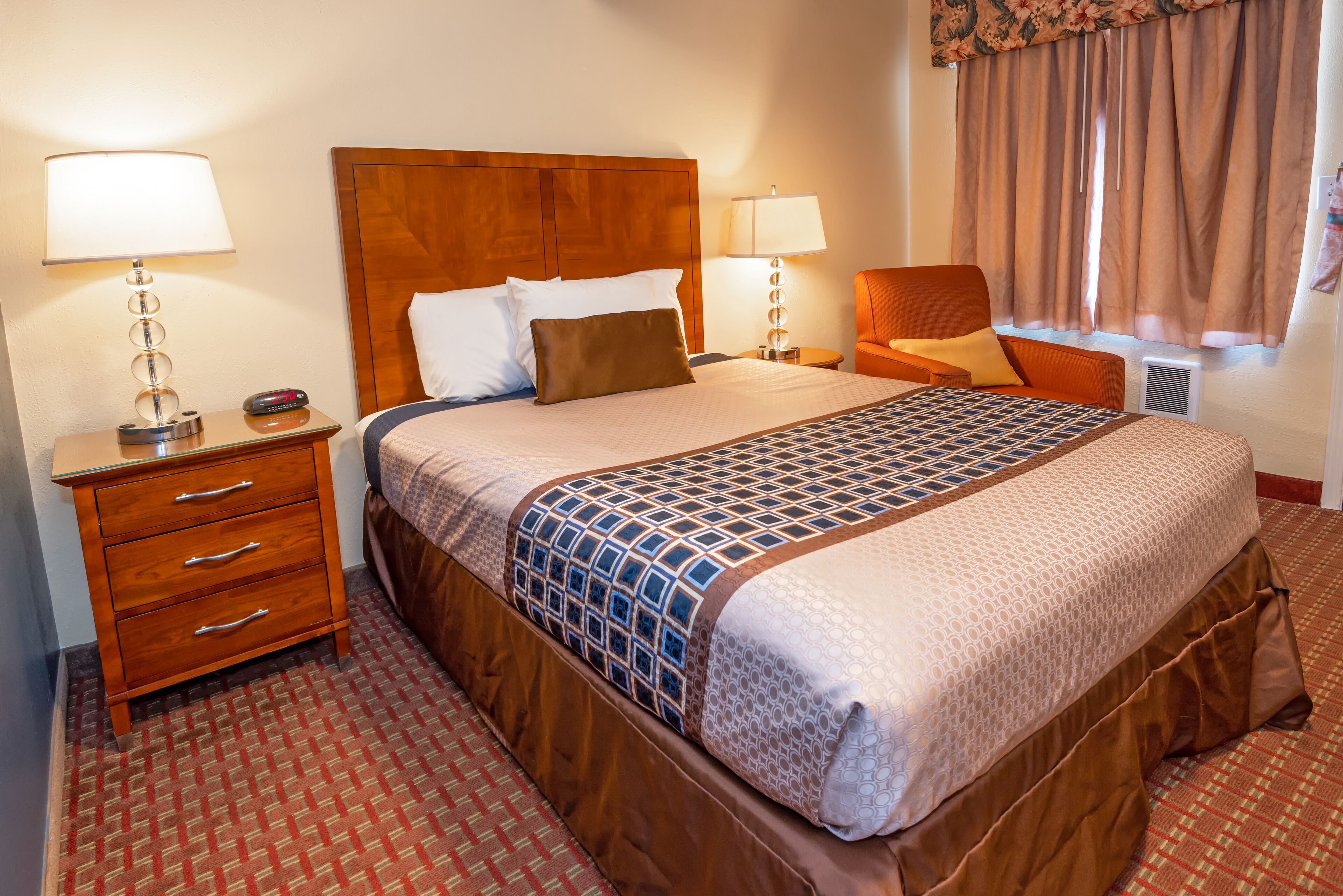A hotel room with a large bed, two bedside tables, a chair, and a window with curtains.