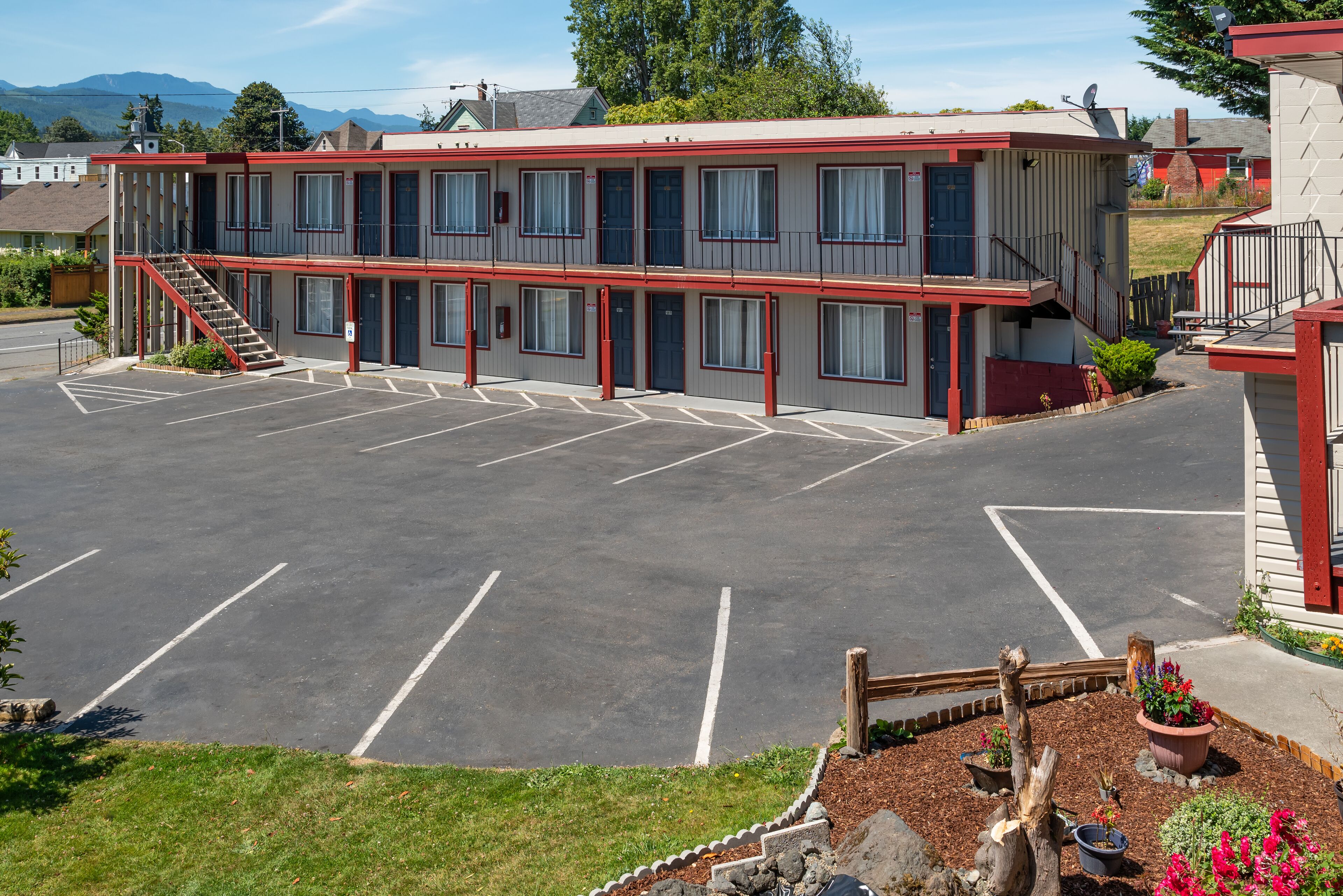 Ein Motel mit Parkplatz, einer Treppe zum Obergeschoss und einem kleinen Garten mit Pflanzen.