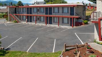 Ein Motel mit Parkplatz, einer Treppe zum Obergeschoss und einem kleinen Garten mit Pflanzen.