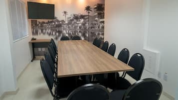 A conference room with a long table, black chairs, a mounted TV, and a cityscape mural on the wall.