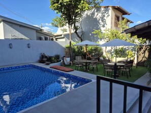 A swimming pool with a tiled edge, surrounded by outdoor furniture and greenery. - Real Hotel (Sete Lagoas)