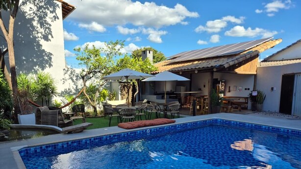 A swimming pool with blue tiles, surrounded by outdoor furniture and umbrellas. - Real Hotel (Sete Lagoas)