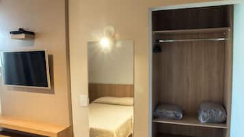 Habitació d'hotel amb llit, televisió, mirall i armari de fusta.