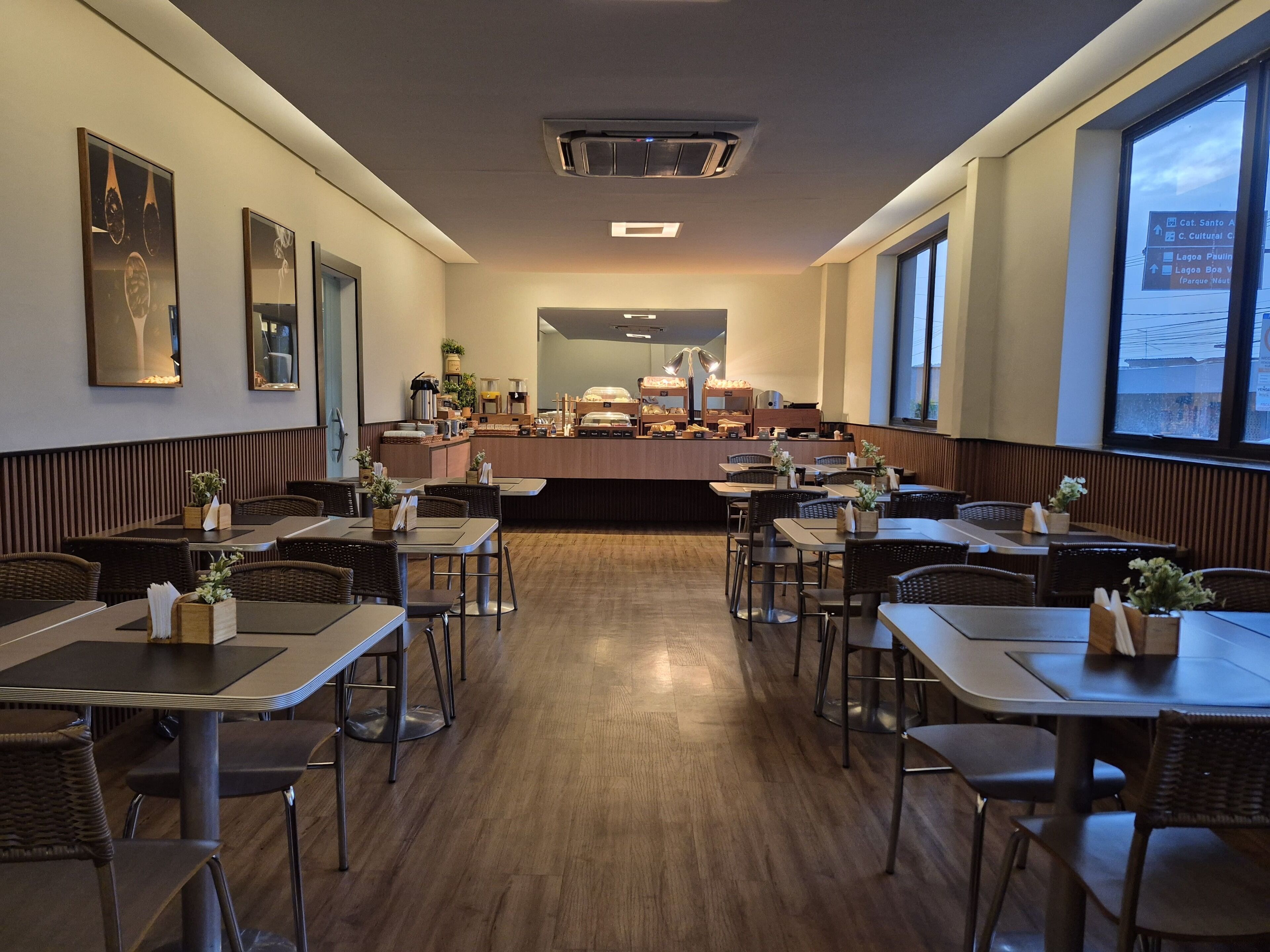 Un restaurante con mostrador central, varias mesas y sillas, y amplios ventanales en un lateral.