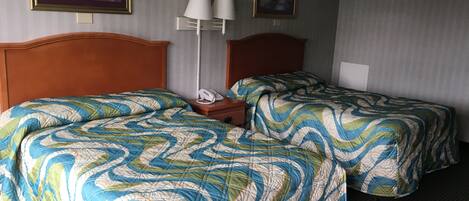 A hotel room with two beds, each with a patterned bedspread, a wooden headboard, a bedside table with a lamp, and two framed pictures on the wall.