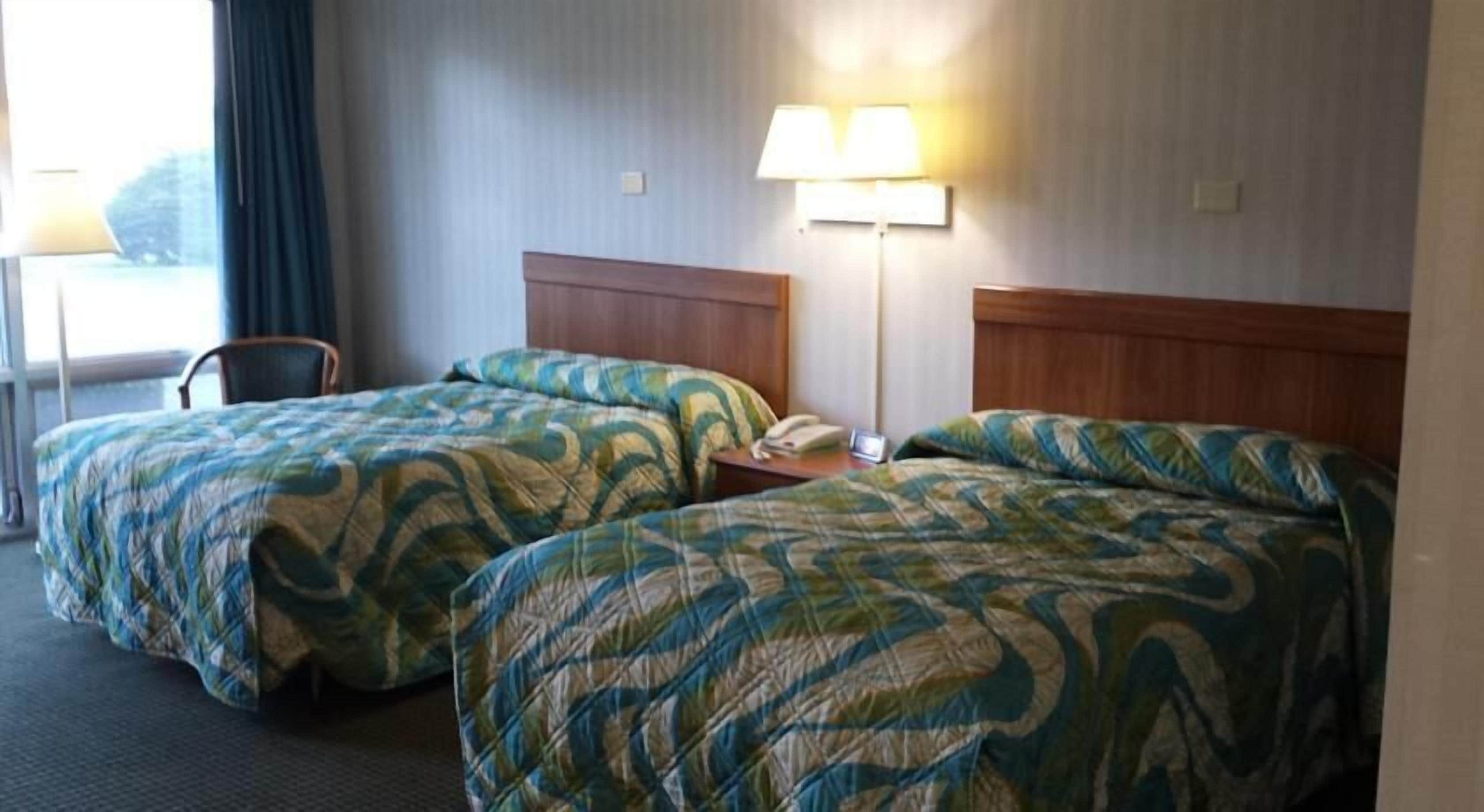 A hotel room with two beds, each with a patterned bedspread, a nightstand with a lamp, and a chair.