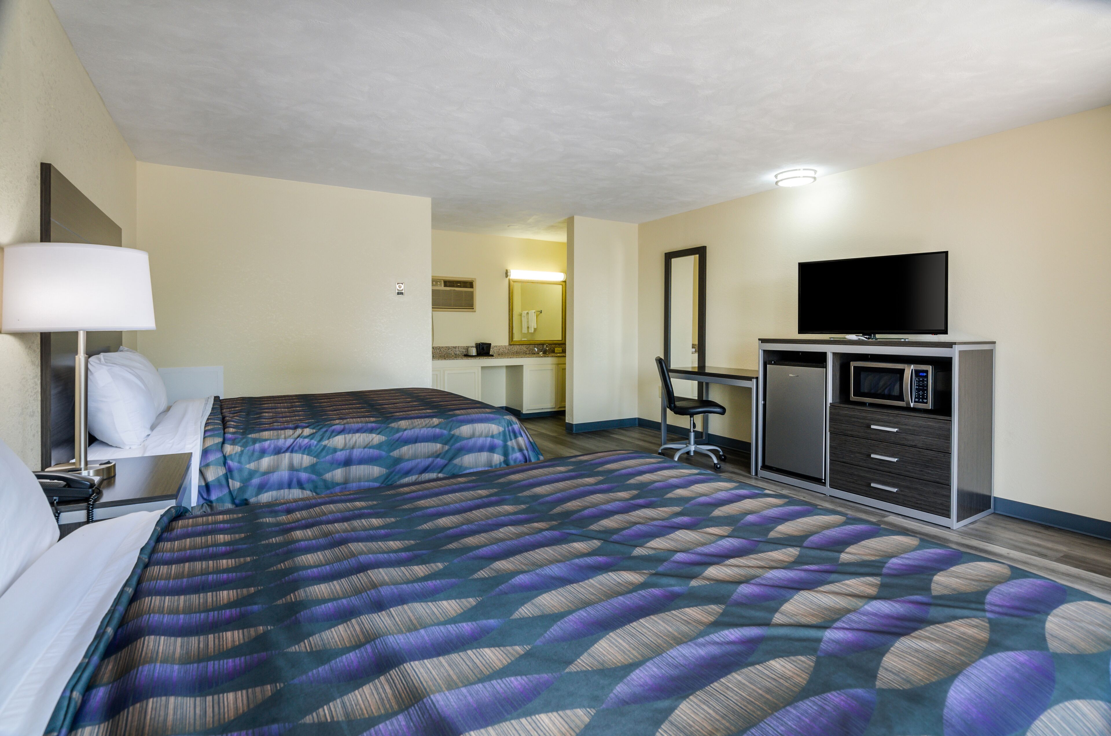 A hotel room with two beds, a desk, a television, and a microwave.