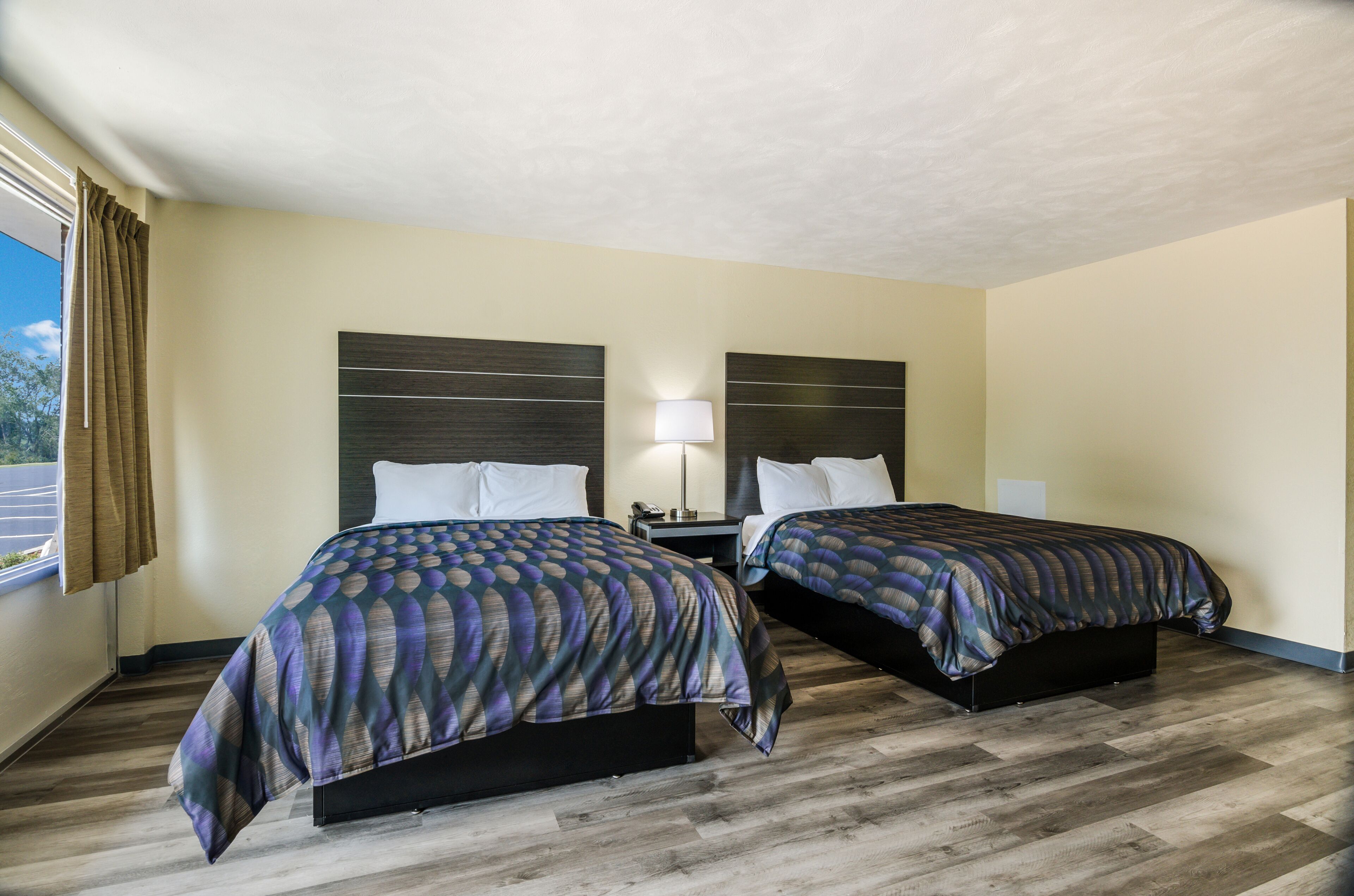 A hotel room with two beds, a nightstand, a lamp, and a window with curtains.